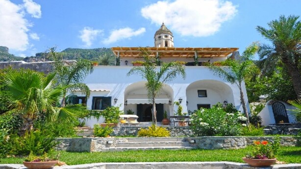A white building with a bell tower, surrounded by palm trees and a stone wall. - Casa Santacroce 2 with large garden (Praiano)