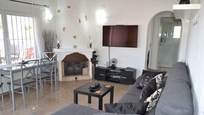 Un soggiorno con un divano grigio, un tavolino, un camino, una televisione a parete e una porta vetrata che dà su un balcone.
