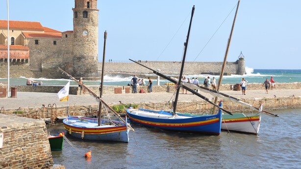 A coastal scene with boats docked near a stone wall and a tower. - Collioure: beautiful apartment classified ***, quiet, swimming pool, garden, private parking (Collioure)