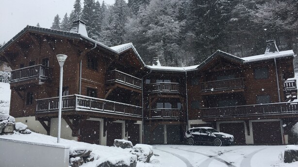Un grand bâtiment en bois doté de nombreux balcons, entouré d’arbres couverts de neige.