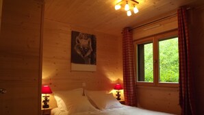 Une chambre à coucher dans un chalet en bois, avec un lit, deux lampes de chevet, une fenêtre avec des rideaux et un tableau représentant un renard accroché au mur.