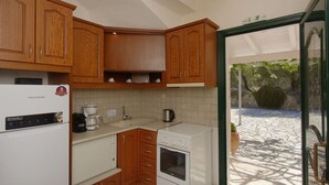 Eine kompakte Küche mit Holzschränken, einem weißen Kühlschrank, einer Kaffeemaschine und einem eingebauten Backofen.