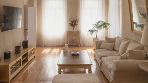 A spacious living room with a high arched ceiling, a central coffee table, a sofa, and a television mounted on the wall. - Oia Mansion 4 Bedroom Villa With Panoramic Sunset View (Santorini)