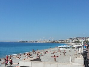 A beach with people sunbathing and swimming, a clear blue sky, and buildings in the background.