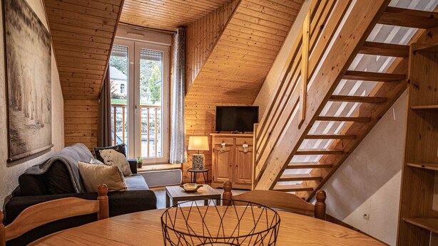 Un acogedor interior de cabaña con techo de madera, una mesa redonda de comedor, un sofá y un televisor sobre un mueble de madera.