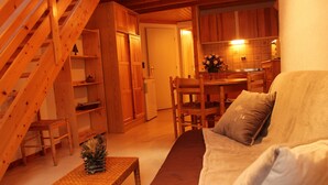 Una sala de estar acogedora con una escalera de madera, una mesa de comedor con sillas y un sofá con cojines.