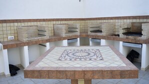 Un patio al aire libre con suelo de baldosas, una mesa central y varias parrillas de ladrillo.