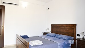 Un dormitorio con una cama de madera, una mesita de noche con lámpara y un equipo de aire acondicionado en la pared.