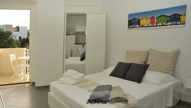 A bedroom with a bed, pillows, a blanket, a mirror, and a painting on the wall. - App. PORTO RUSSO♡ Splendid studio apartment (Otranto)