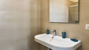 A bathroom with a white sink, a mirror, and beige tiled walls. - App. PORTO RUSSO♡ Splendid studio apartment (Otranto)