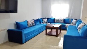A living room with a blue sectional sofa, a wooden coffee table, and a flat-screen TV mounted on the wall. - Beautiful apartment in Essaouira 4263 (Essaouira)