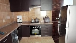 A compact kitchen with dark cabinets, a stainless steel refrigerator, a washing machine, and a small oven. - Beautiful apartment in Essaouira 4263 (Essaouira)