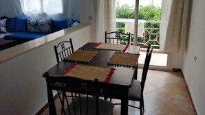 A dining area with a table set for four, two chairs on each side, and a window overlooking a balcony. - Beautiful apartment in Essaouira 4263 (Essaouira)