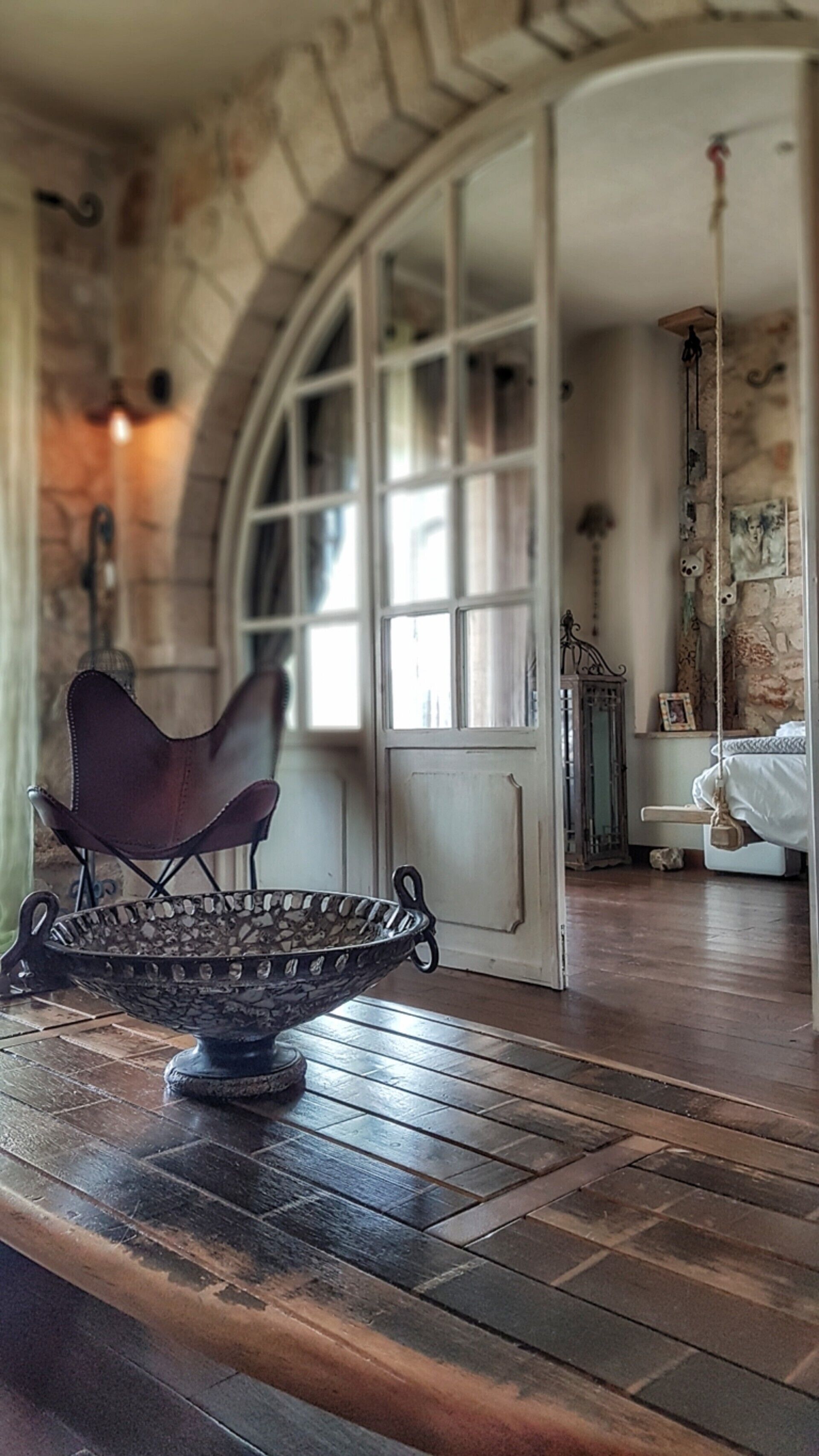 Una habitación con suelo de madera, un bol de metal sobre una mesa, una silla y una cama con cubrecama blanco.