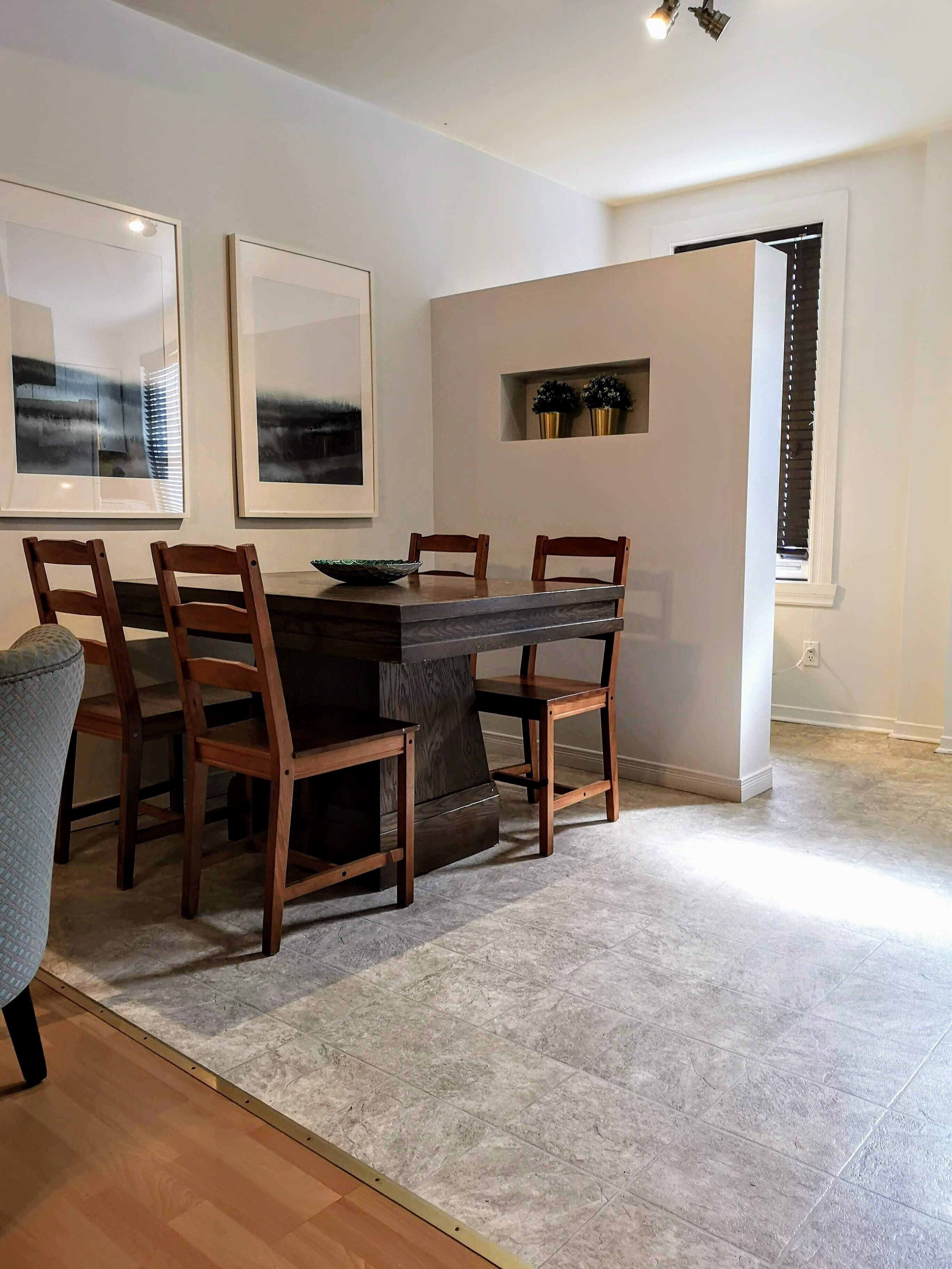 Un coin repas comprenant une table rectangulaire, six chaises en bois et deux œuvres d’art encadrées accrochées au mur.