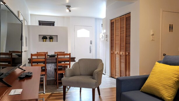 Uma sala de estar com sofá, poltrona, mesa de jantar de madeira e cadeiras.