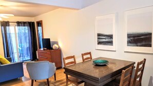 Uma sala de estar moderna com área de jantar, destacando uma mesa de madeira, cadeiras, um sofá e uma TV sobre um armário de madeira.