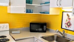 Uma cozinha compacta com armários brancos, micro-ondas, pia e fogão.