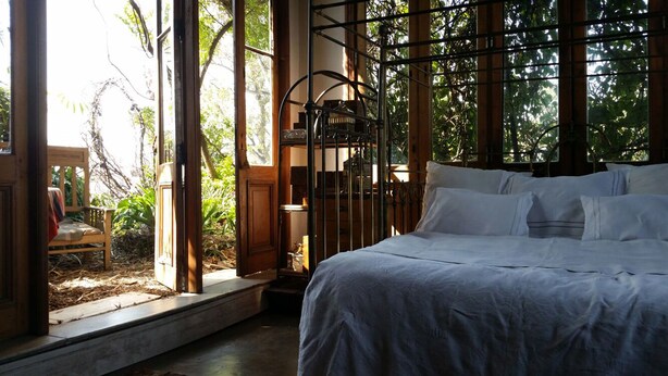 Un dormitorio con cama, ventana con vista a zonas verdes y una silla al exterior.