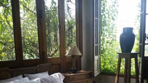 Un dormitorio con cama, mesita de noche, lámpara, cómoda y ventana con vista a árboles.