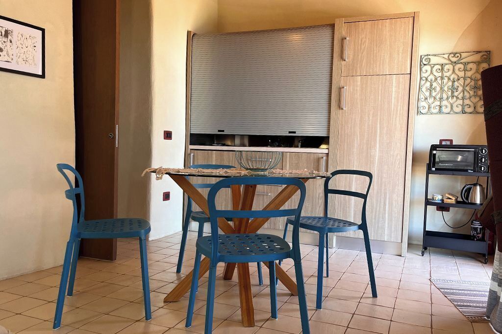 A compact kitchen with a dining table and four chairs, a built-in oven, and a small refrigerator.