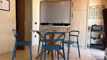 A compact kitchen with a dining table and four chairs, a built-in oven, and a small refrigerator.