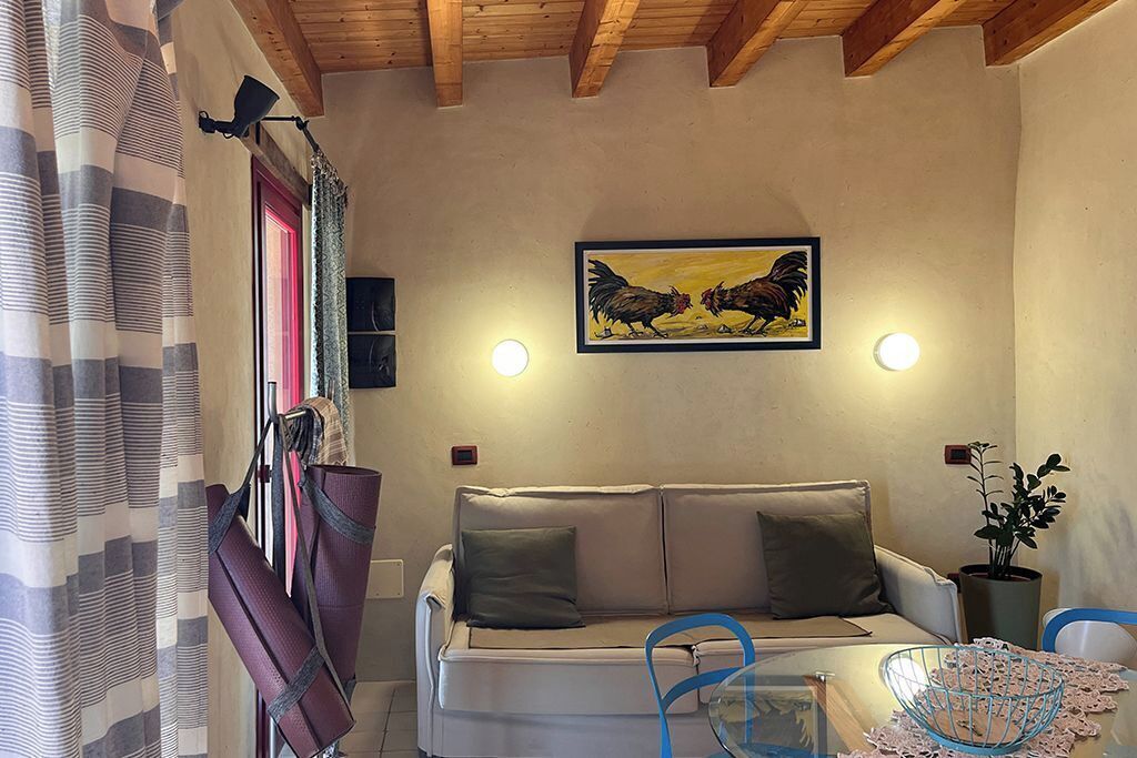 Un soggiorno con divano, tavolo, sedia, quadro con galli e una pianta in vaso.