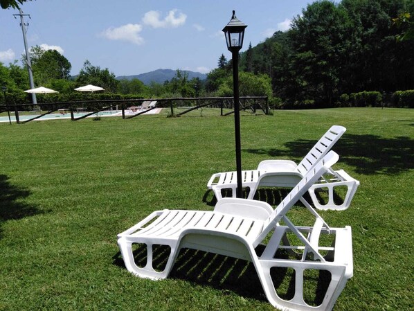A grassy area with white lounge chairs and a lamp post.