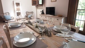 A dining area with a wooden table set for a meal, white chairs, and a television on a cabinet. - CASALE LA FATA, SMEMORINA splendid apartment facing the pool, sleeps 5 (camaiore)