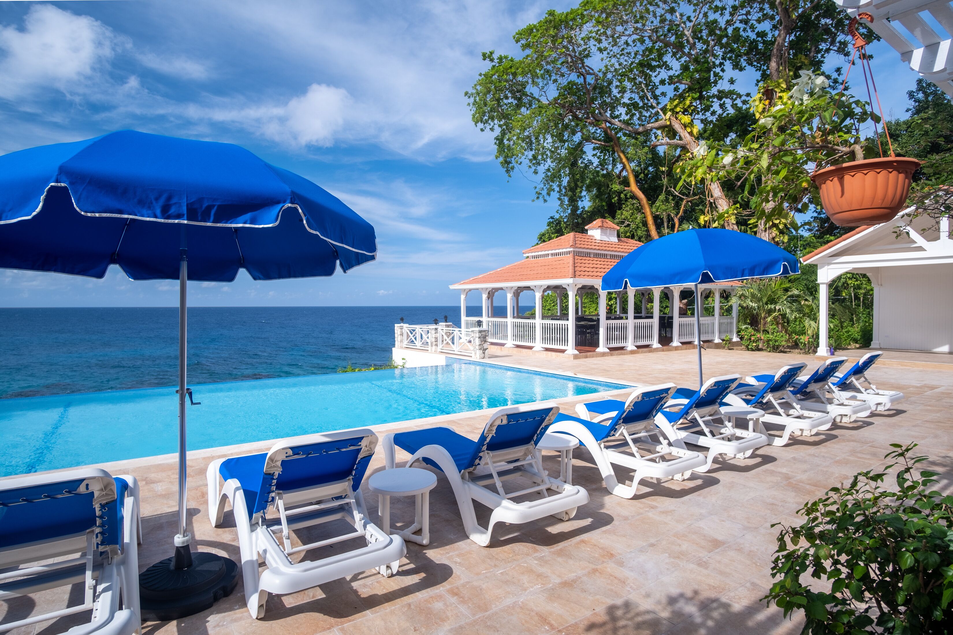 A poolside area with blue umbrellas, lounge chairs, and a view of the ocean.