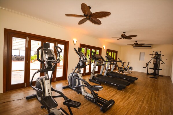 A gym with treadmills, ellipticals, and stationary bikes, wooden floors, and ceiling fans. - Luxury 13-bedroom, 7-acre, oceanfront villa, with all-inclusive option. (Ocho Rios)