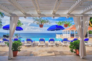 A sunlit outdoor lounge area with blue chairs and umbrellas, overlooking a pool and the sea. - Luxury 13-bedroom, 7-acre, oceanfront villa, with all-inclusive option. (Ocho Rios)