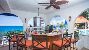 Eine Bar mit Meerblick, inklusive Bar, Stühle und Deckenventilator.