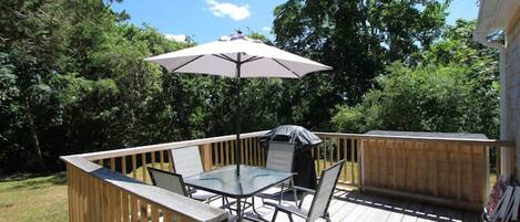 A wooden deck with a glass table and chairs, an umbrella, and a barbecue grill.