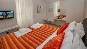 Une chambre d’hôtel avec un lit, une télévision, un miroir et une table de chevet sur laquelle se trouve un plateau de fruits.