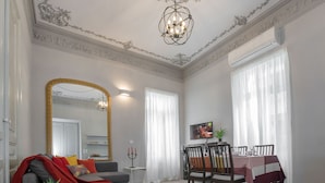 Un salon spacieux agrémenté d’un grand miroir, un coin repas avec une table dressée pour deux personnes et un lustre moderne.