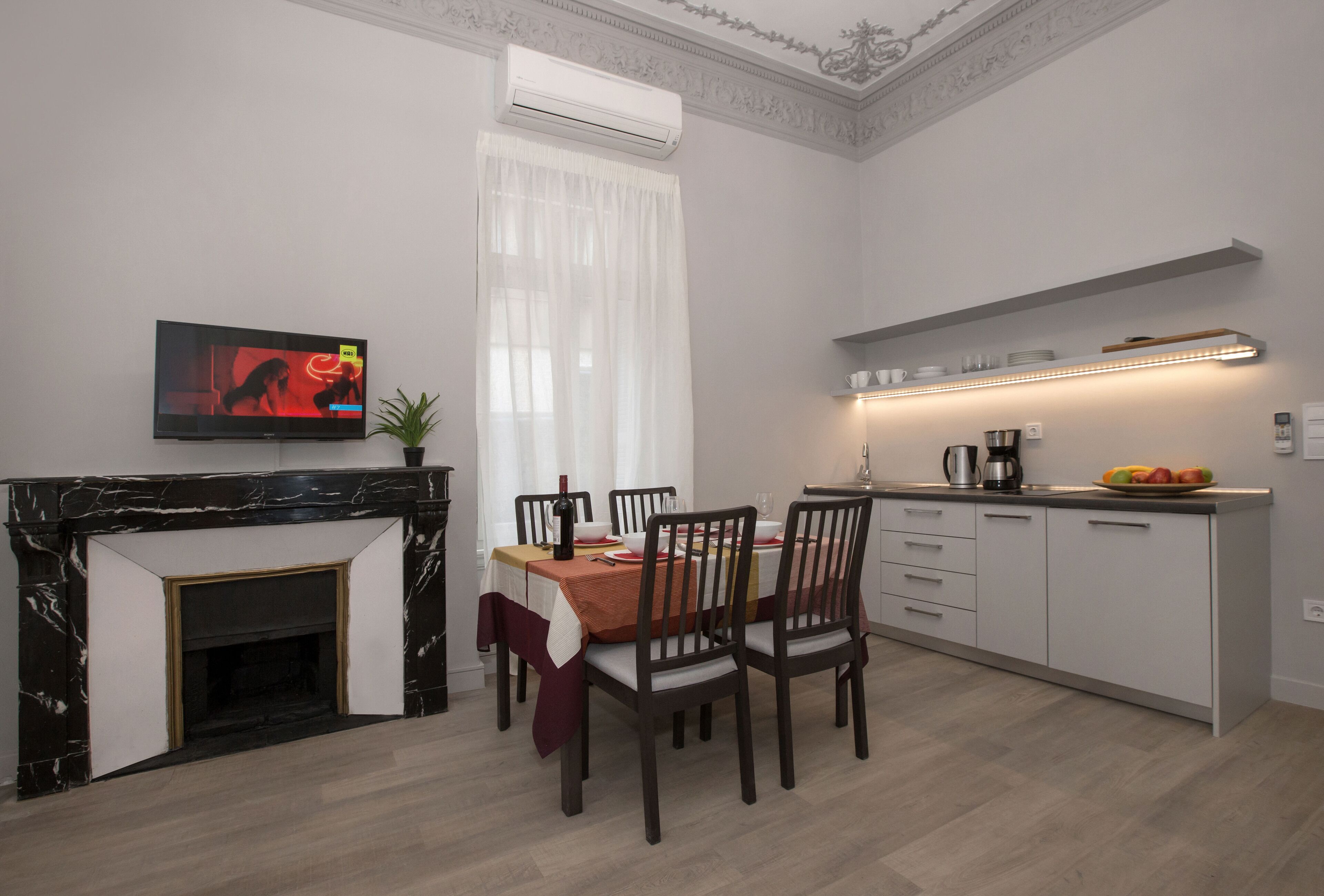 A modern kitchen with a dining area, featuring a TV, fireplace, and a fruit bowl on the counter.