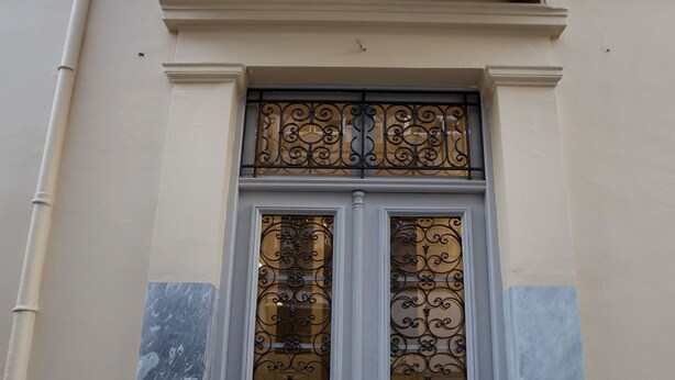 Une façade d’immeuble avec une double porte ornée de ferronnerie ouvragée et un balcon doté de balustrades décoratives.