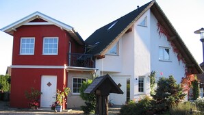 Een tweelaags huis met een rood-wit gevel, een balkon en een tuin met potplanten.