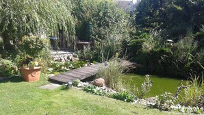 Een tuin met een houten brug over een vijver, omgeven door verschillende planten en bomen.