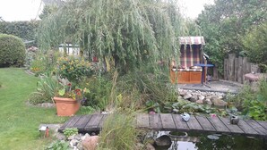 Een tuin met een houten terras, een vijver en een zitgedeelte met een geruit bankje.