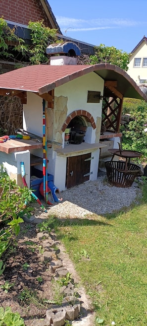 Un four extérieur en briques, doté d’une cheminée en pierre, entouré d’une zone recouverte de gravier et de verdure.