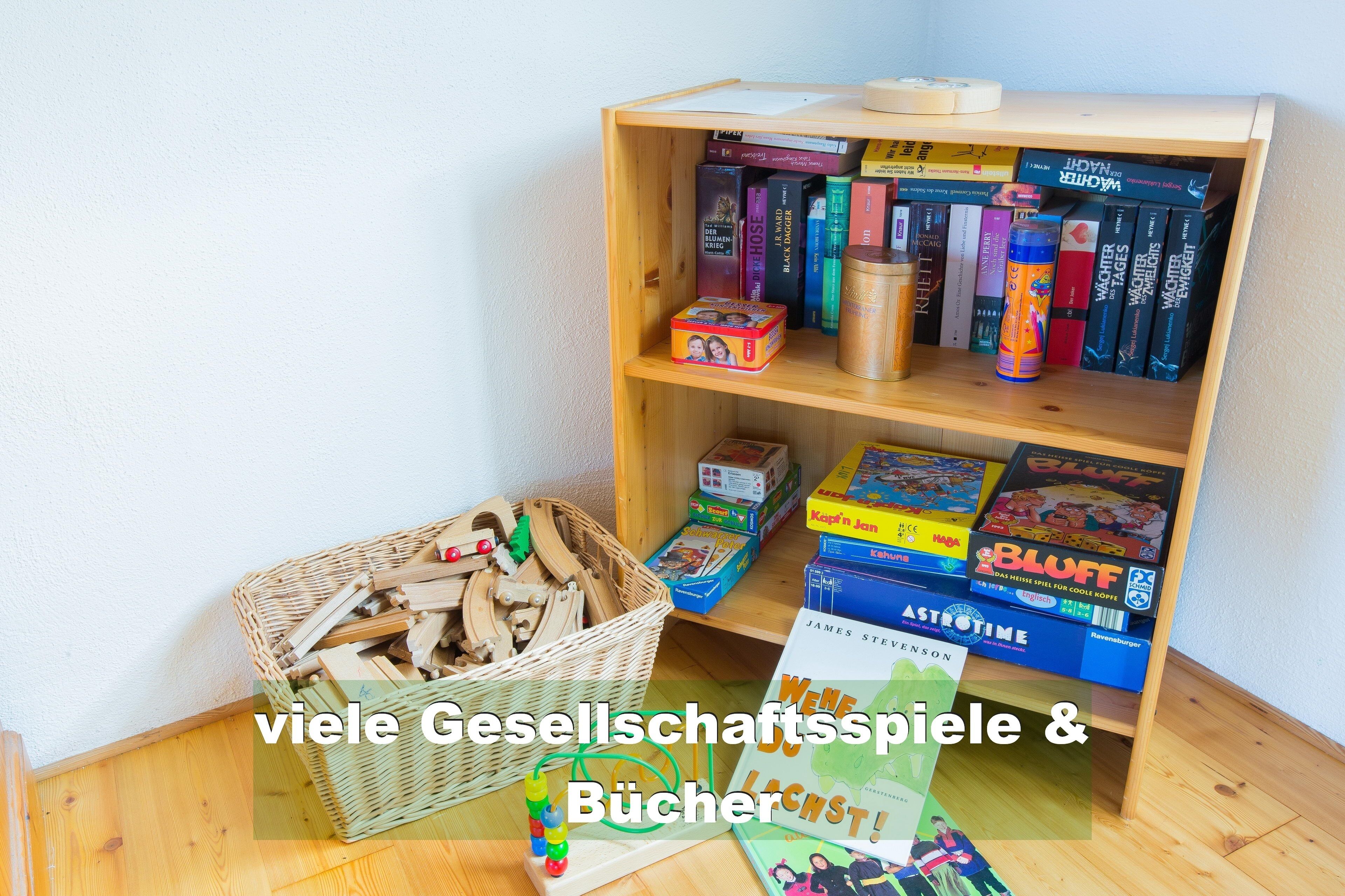 A room with a wooden bookshelf filled with books and games, a wicker basket with items, and a small table with a book and a toy.