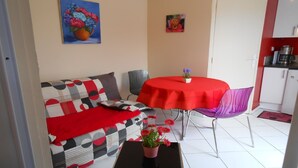 A compact living space with a sofa, a dining table with a red tablecloth, and a small kitchen area. - Charming little Gite C (Sotteville-lès-Rouen)