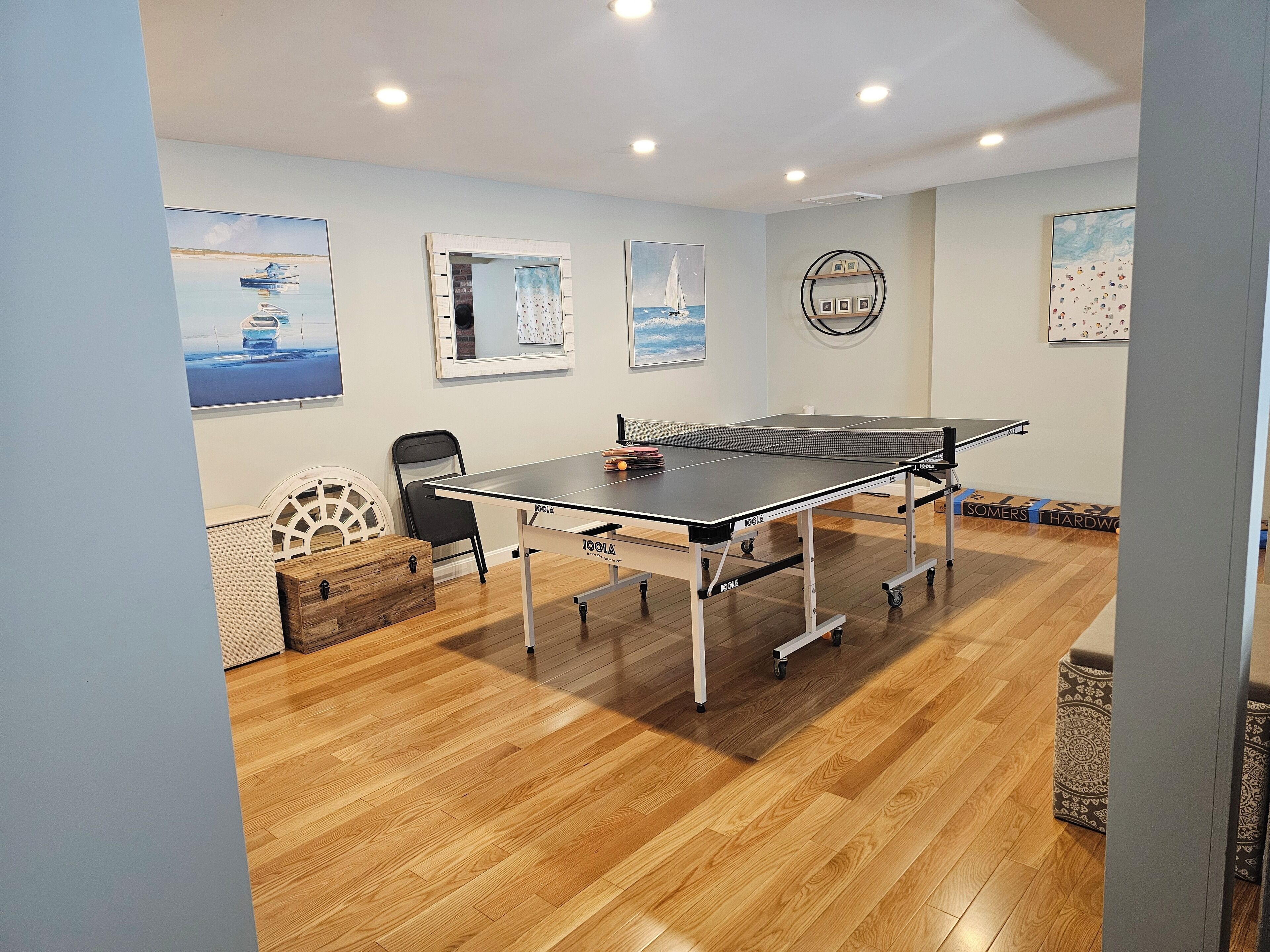 A ping pong table in a room with wooden flooring, a chair, and a small cabinet.