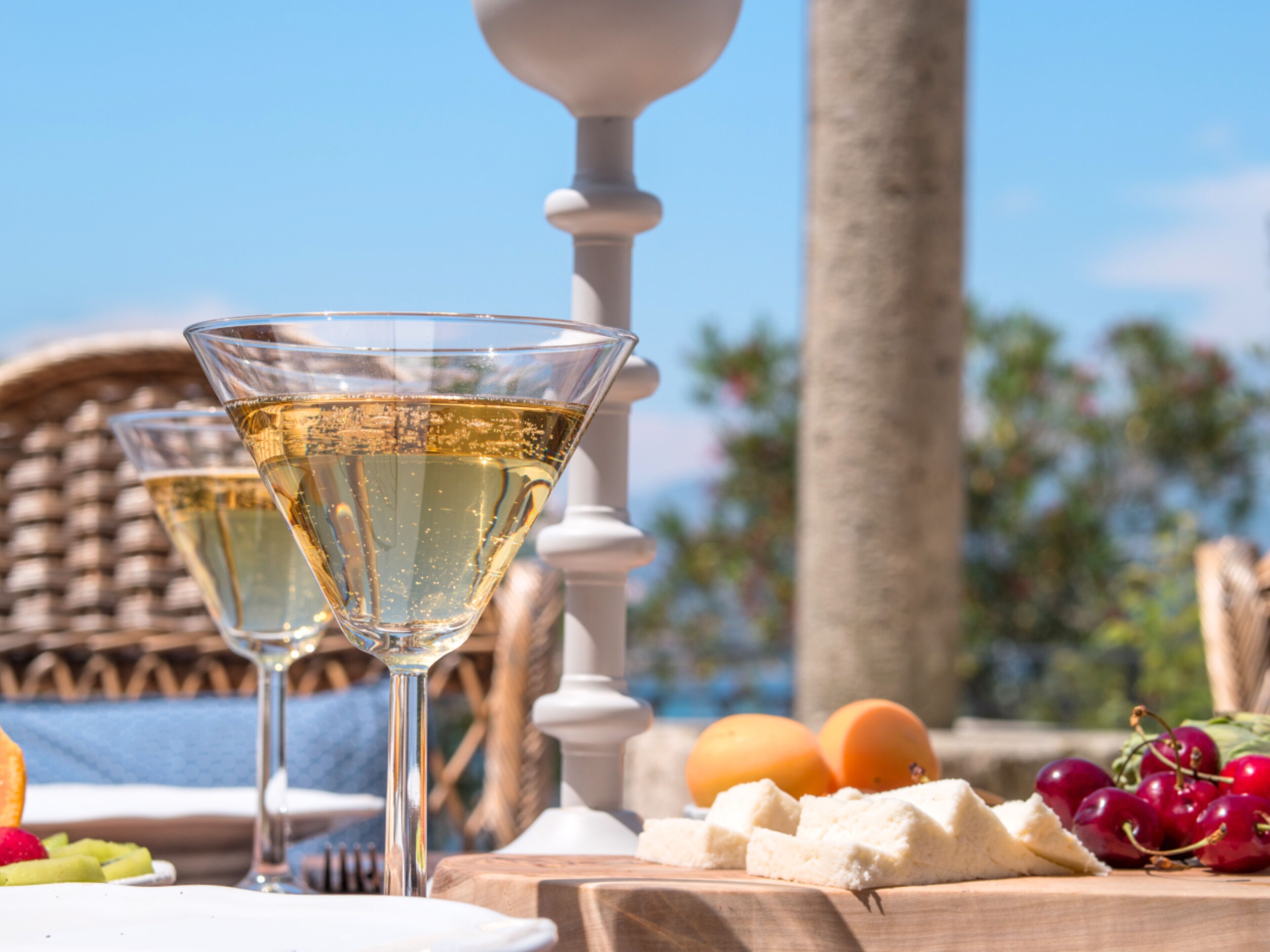 Deux verres de vin blanc sur une table en bois, accompagnés de fruits et de fromage.