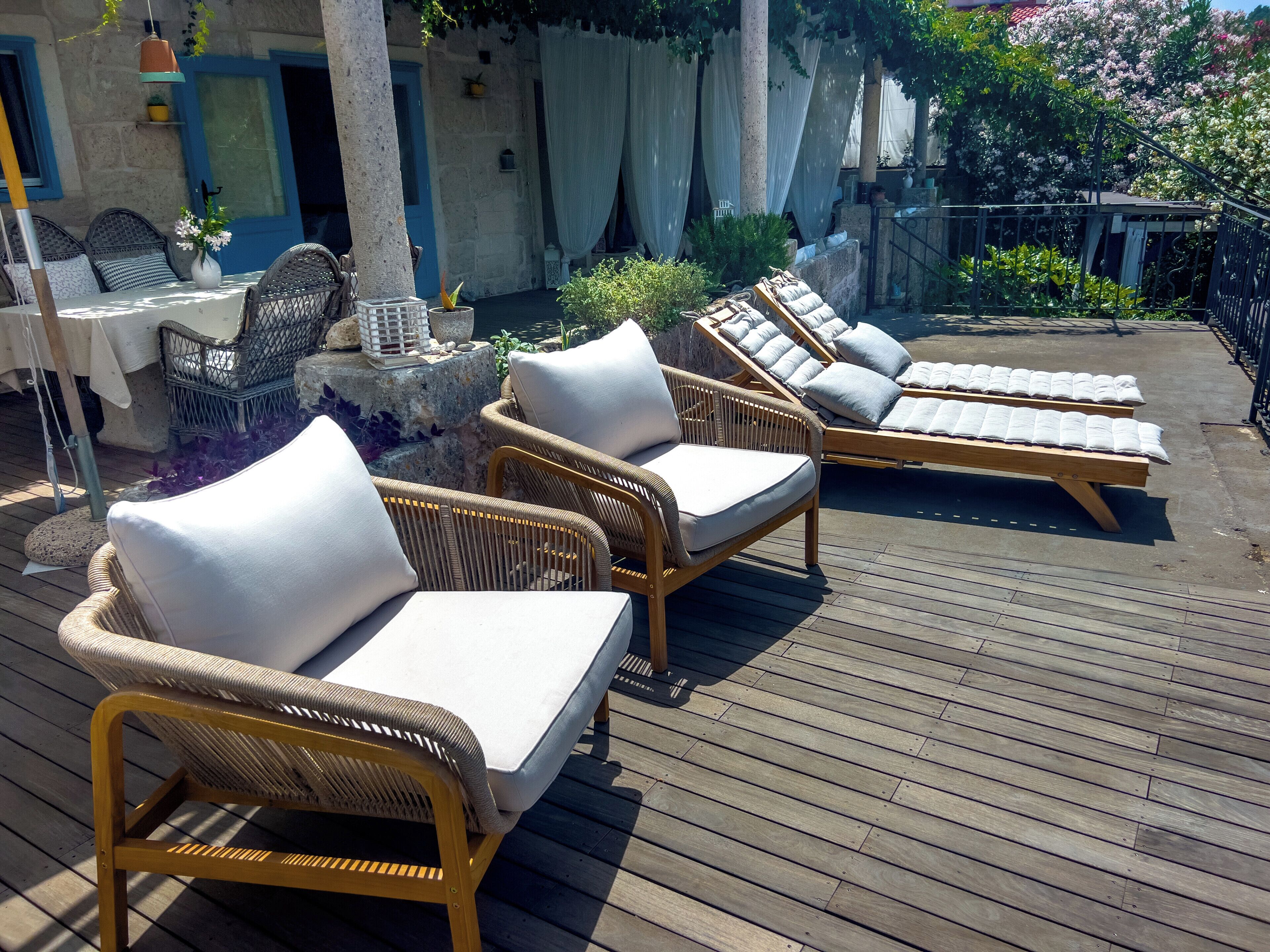 Une terrasse en bois avec des fauteuils de jardin en osier et une table entourée de chaises.