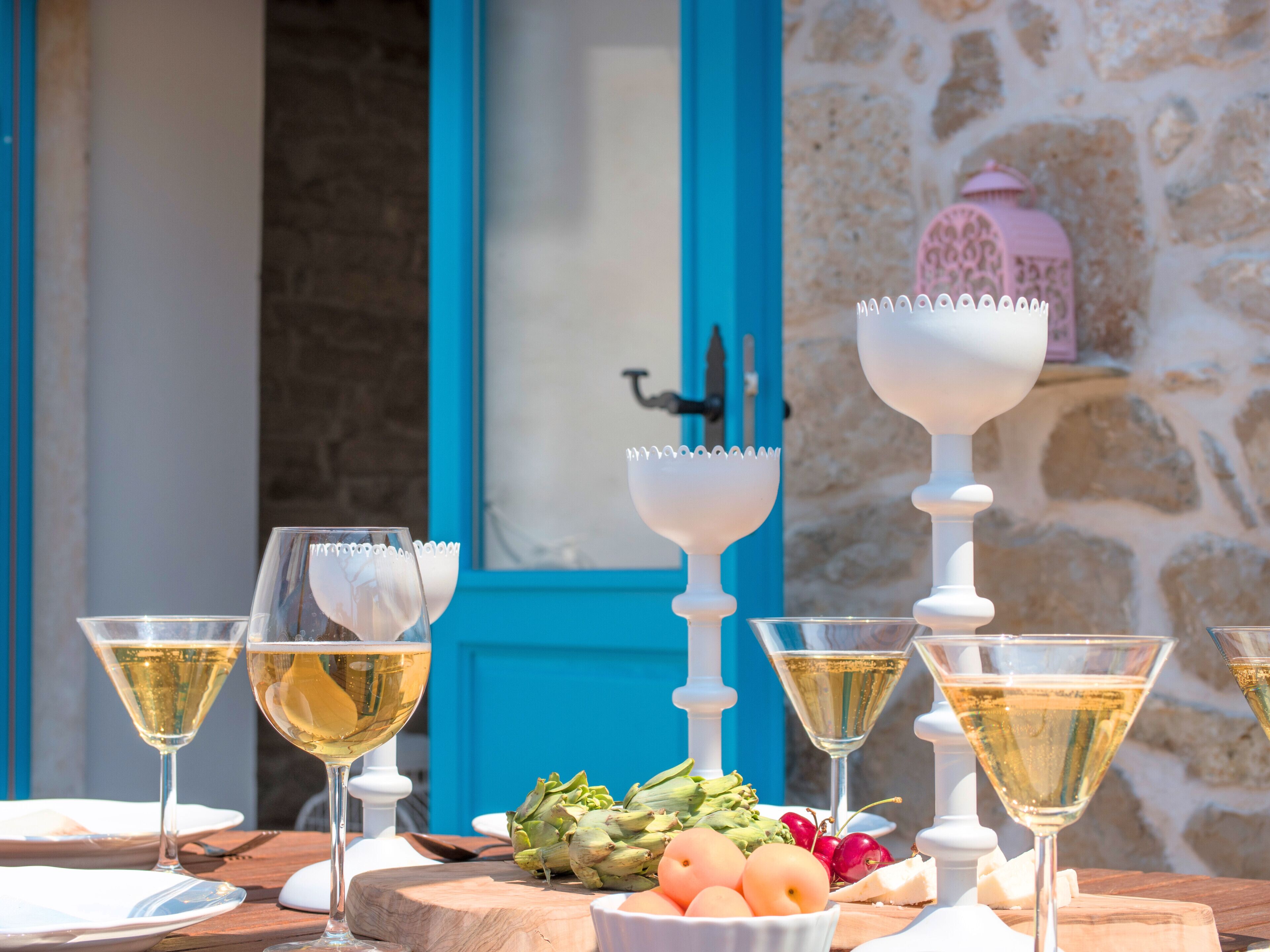 A table set with wine glasses, artichokes, and eggs, with a stone wall and a blue door in the background.
