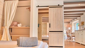 Ein Schlafzimmer mit einem Bett, einer Schiebetür, Holzboden und Blick in einen anderen Raum.