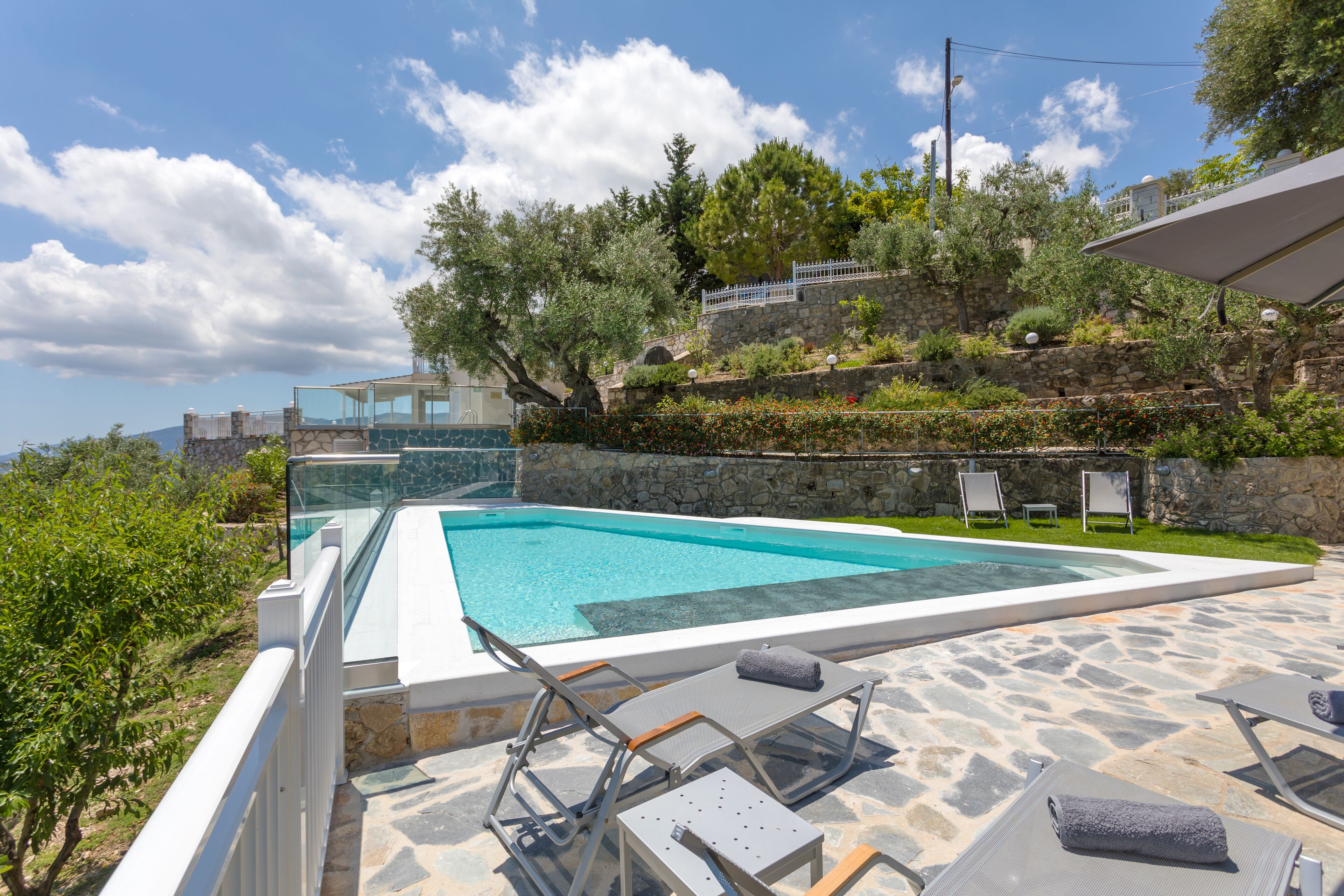 A swimming pool with clear blue water, surrounded by stone steps and lounge chairs.